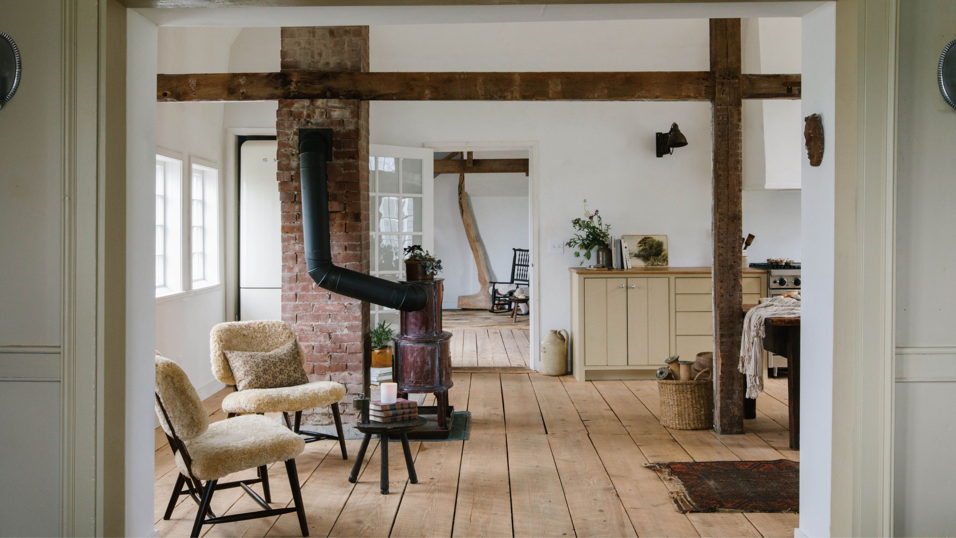 a farmhouse living room with wide plank floorboards timber beams and a fireplace