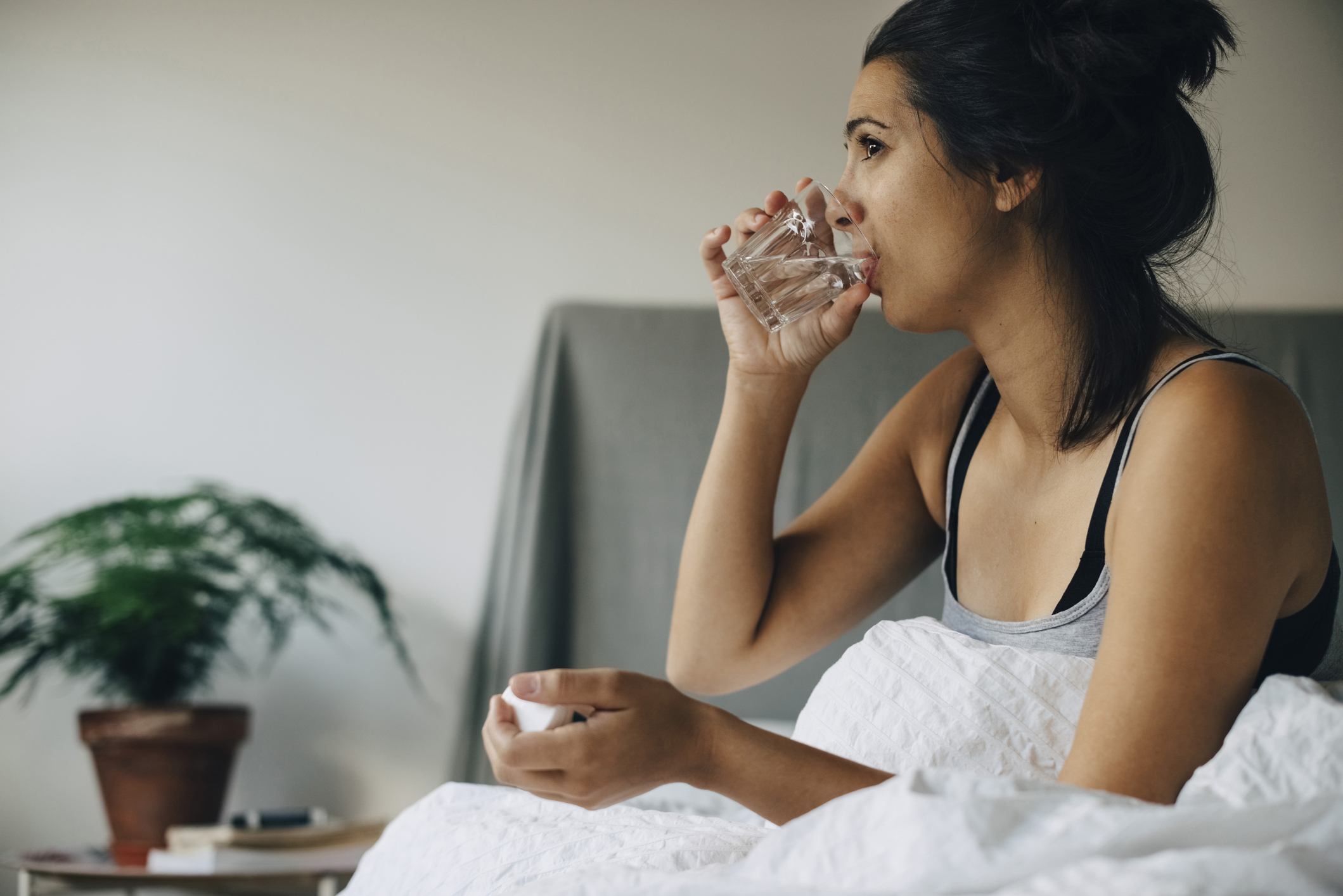 Norovirus symptoms: Woman taking medicine while sitting on bed at home
