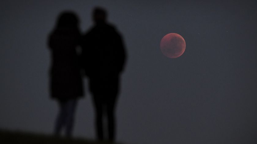 two people stand and look at the blood moon lunar eclipse on the right.