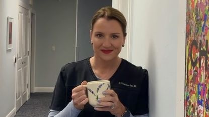 Woman in physician's blue smock holds mug