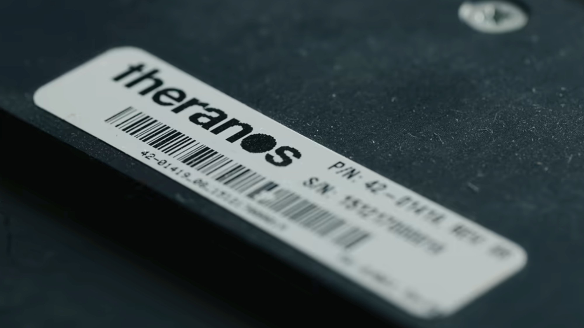 A close up of a label that reads "Theranos" that is attached to one of the parts of the machine seen in You Can See Everything