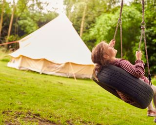 girl on tyre swing in garden with tent in the background