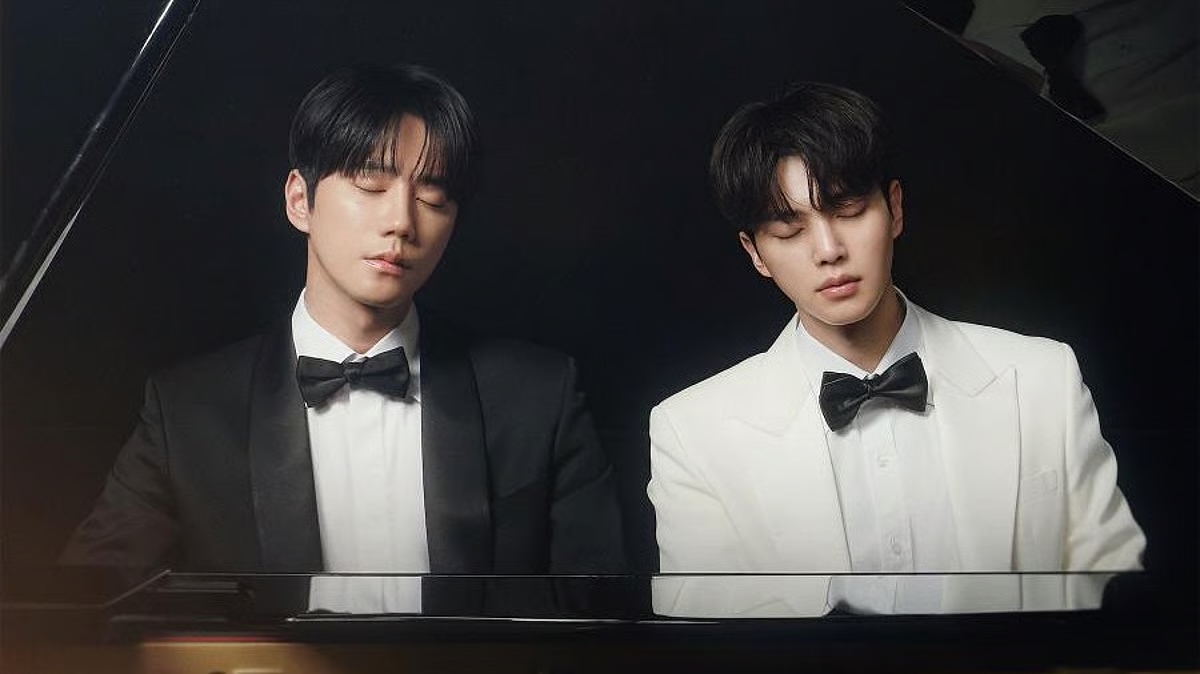 Two man (actors Lee Jun-young and Song Kang) wear tuxedos while sitting behind a piano, in the Korean drama 'Four Hands, Two Sonatas.'