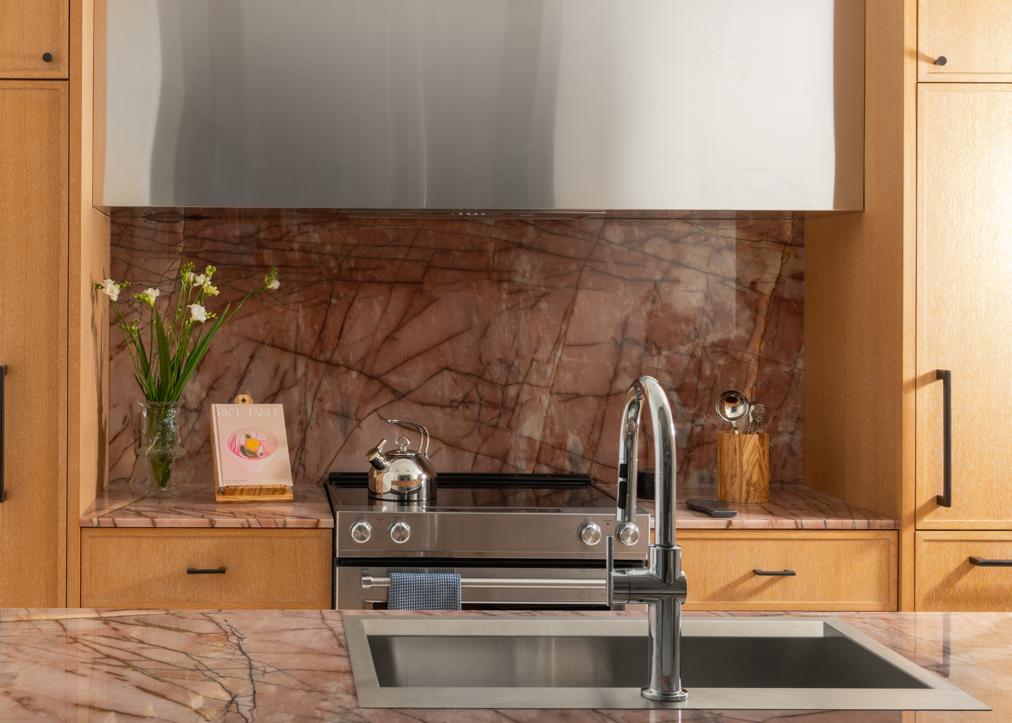 kitchen close up with warm oak cabinets and stainless steel accents and pink marble counters and backsplash