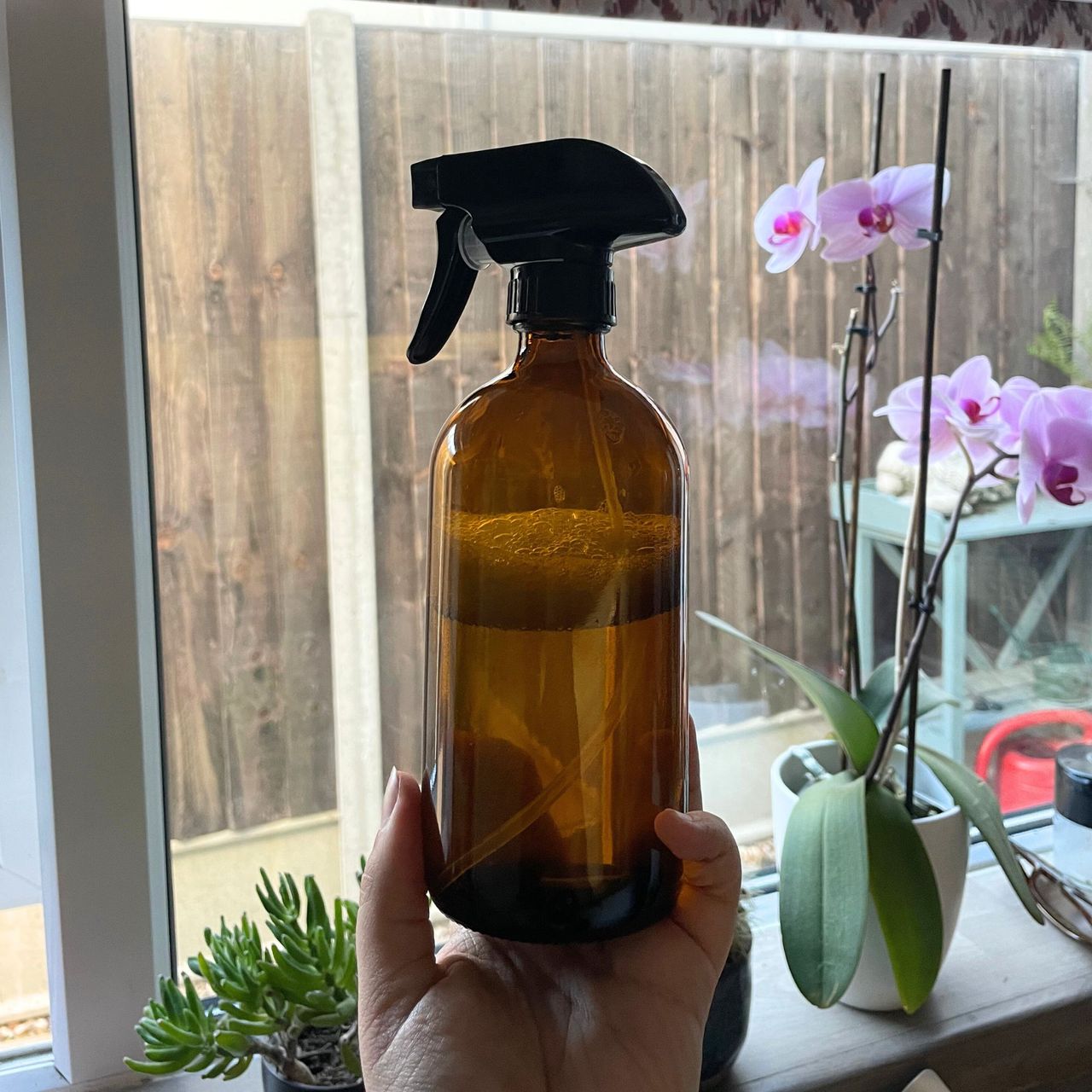 Brown glass bottle with a black spray lid, liquid is visible through the bottle with a layer of bubbles on the top.