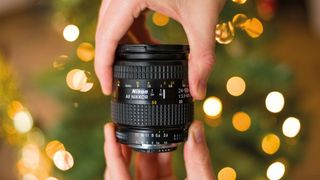 Hand holding a vintage Nikon AF Nikkor 24-50mm lens in front of a bokeh-filled background