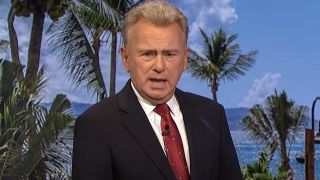 Pat Sajak in black suit and red tie hosting game of Wheel of Fortune