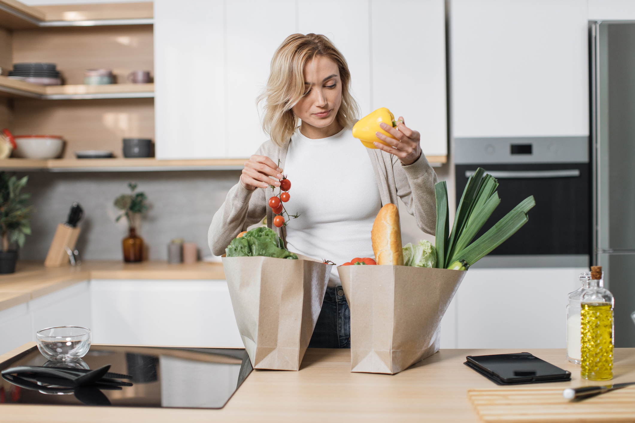 woman holding grocery shopping bag with vegetables standing in the modern light kitchen