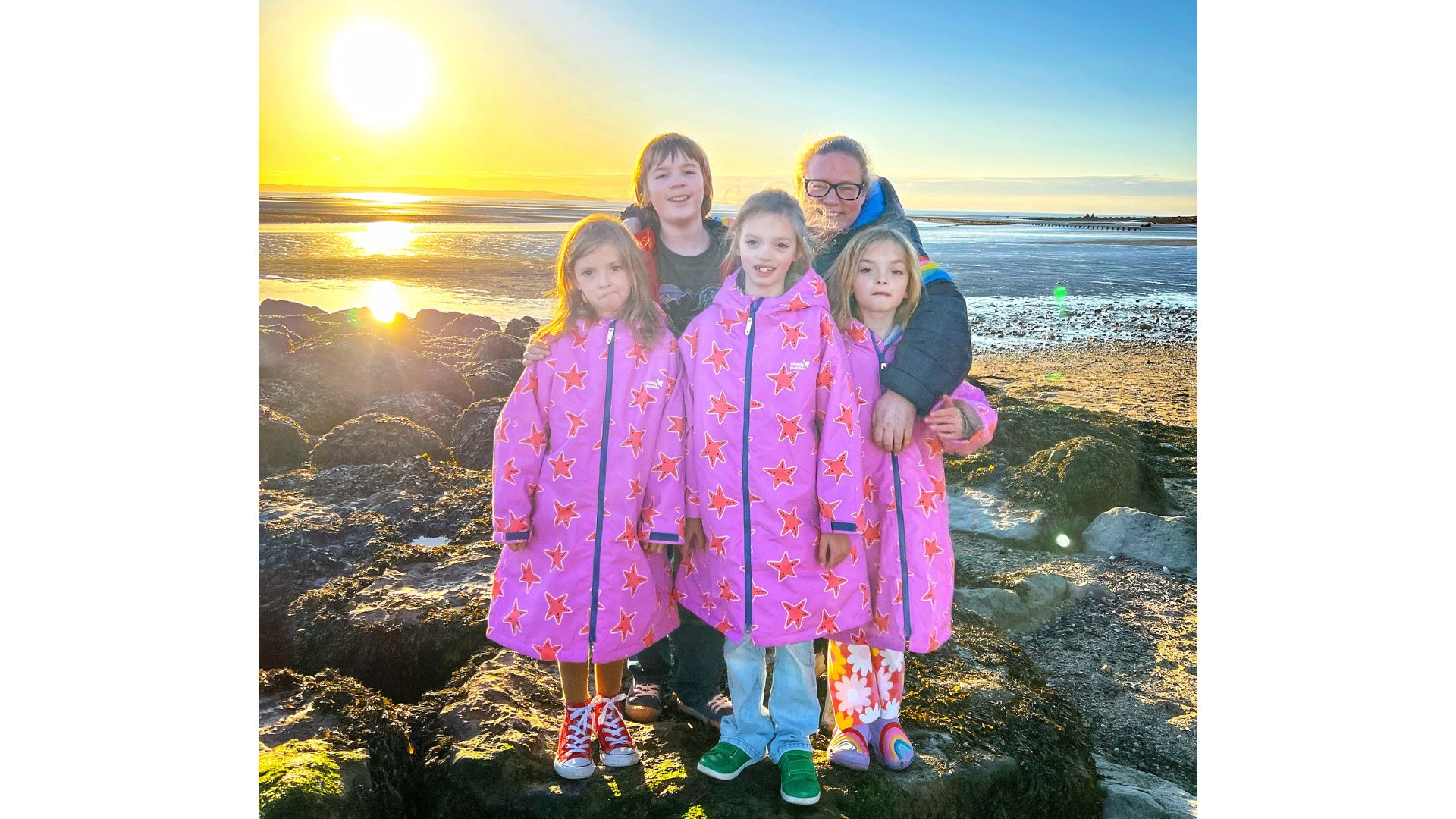 Rebecca Wooldridge on a rocky beach at sunset with her triplet daughters and her son, all wearing dry robes