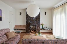 A modern take on a seventies style living room with a chimney breast tiled fully in brown tiles, a bench built in one side and a shelf the other. two sofas in and L-shape just infront with a coffee table and a big paper pendant lamp.