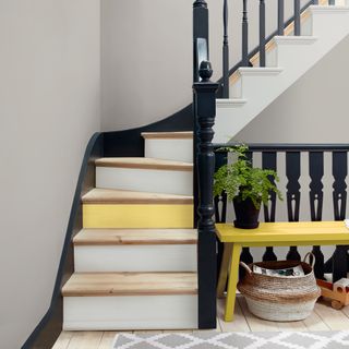 stair case with black railing and wooden floor and yellow bench and pots