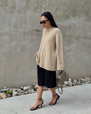 Dawn wears a beige sweater, black skirt, and black sandals.