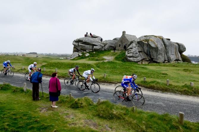 Riders pass through in front of the remains at seaside road in Brittany