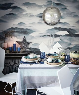 A grey and blue Christmas-themed dining area with printed mountain motif wallpaper, star decor and geometric plastic chairs