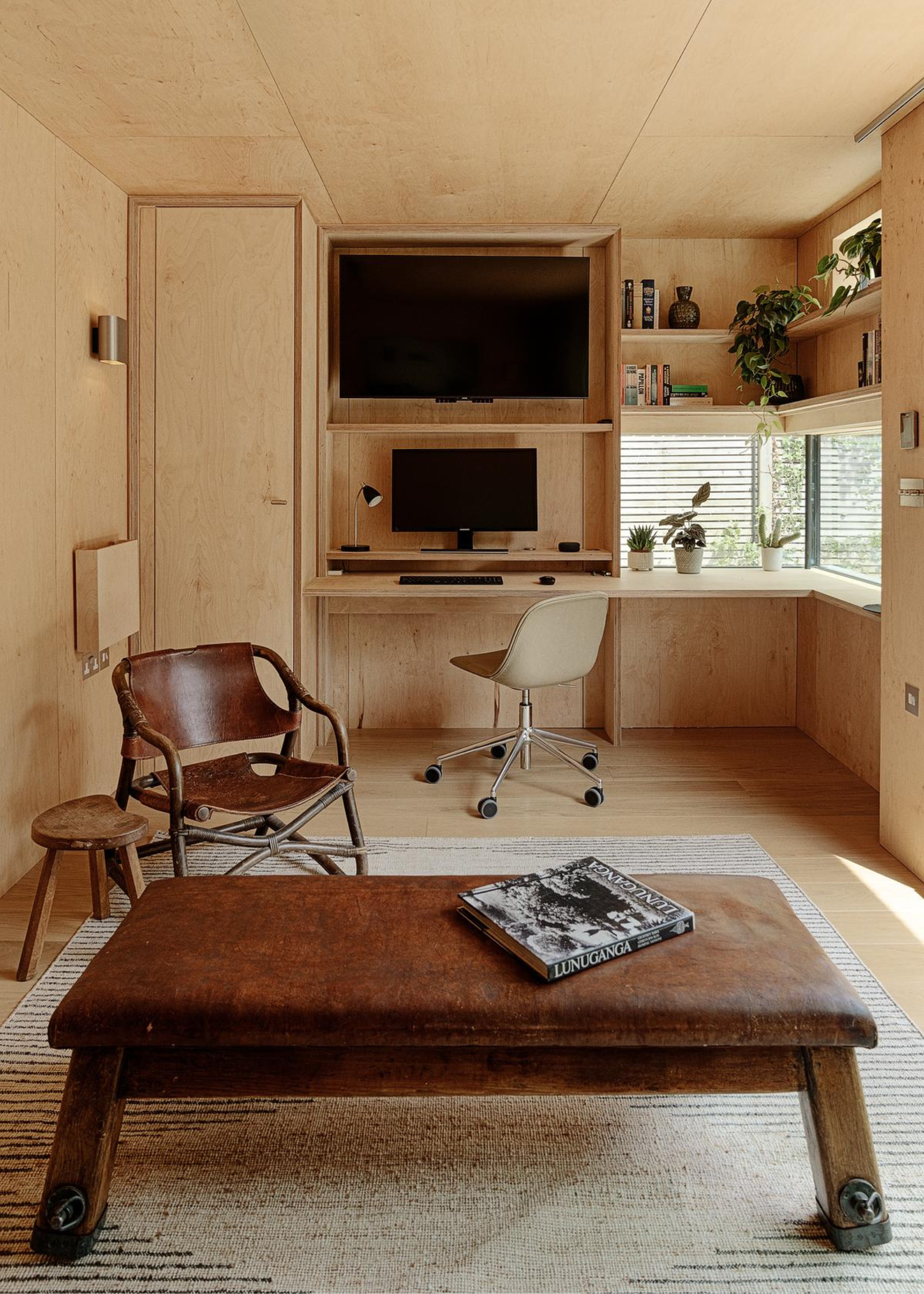 A wooden-clad room with a tv, study area, leather coffee table, and a leather chair