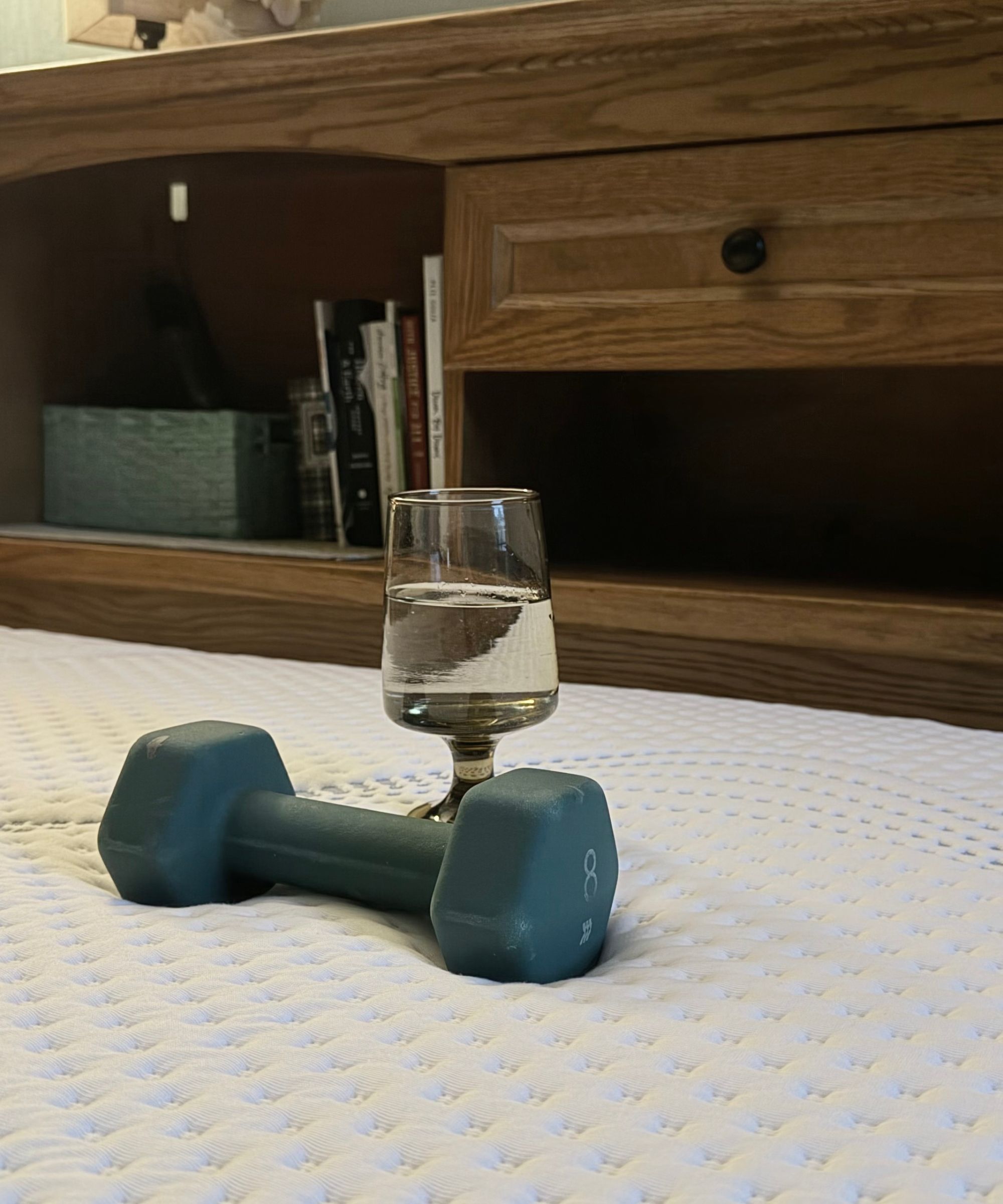 Testing the motion isolation of the Sleep Number ComfortNext with a wine glass filled with water and a blue weight. Behind is a wooden headboard with books.
