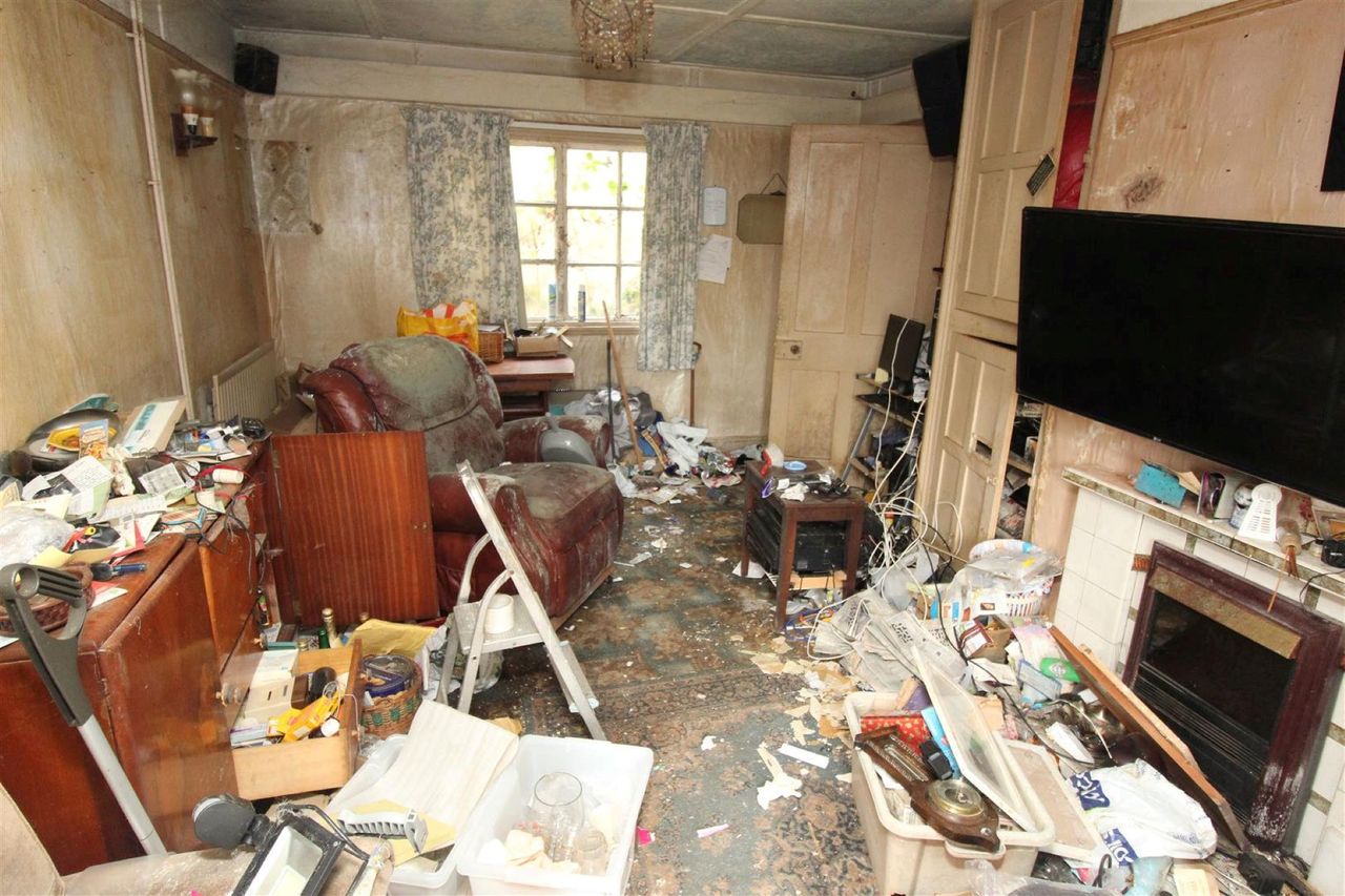 The seperate living room shows a tv and armchair surrounded by rubbish