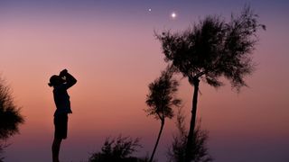 A man stargazing with binoculars at dusk.