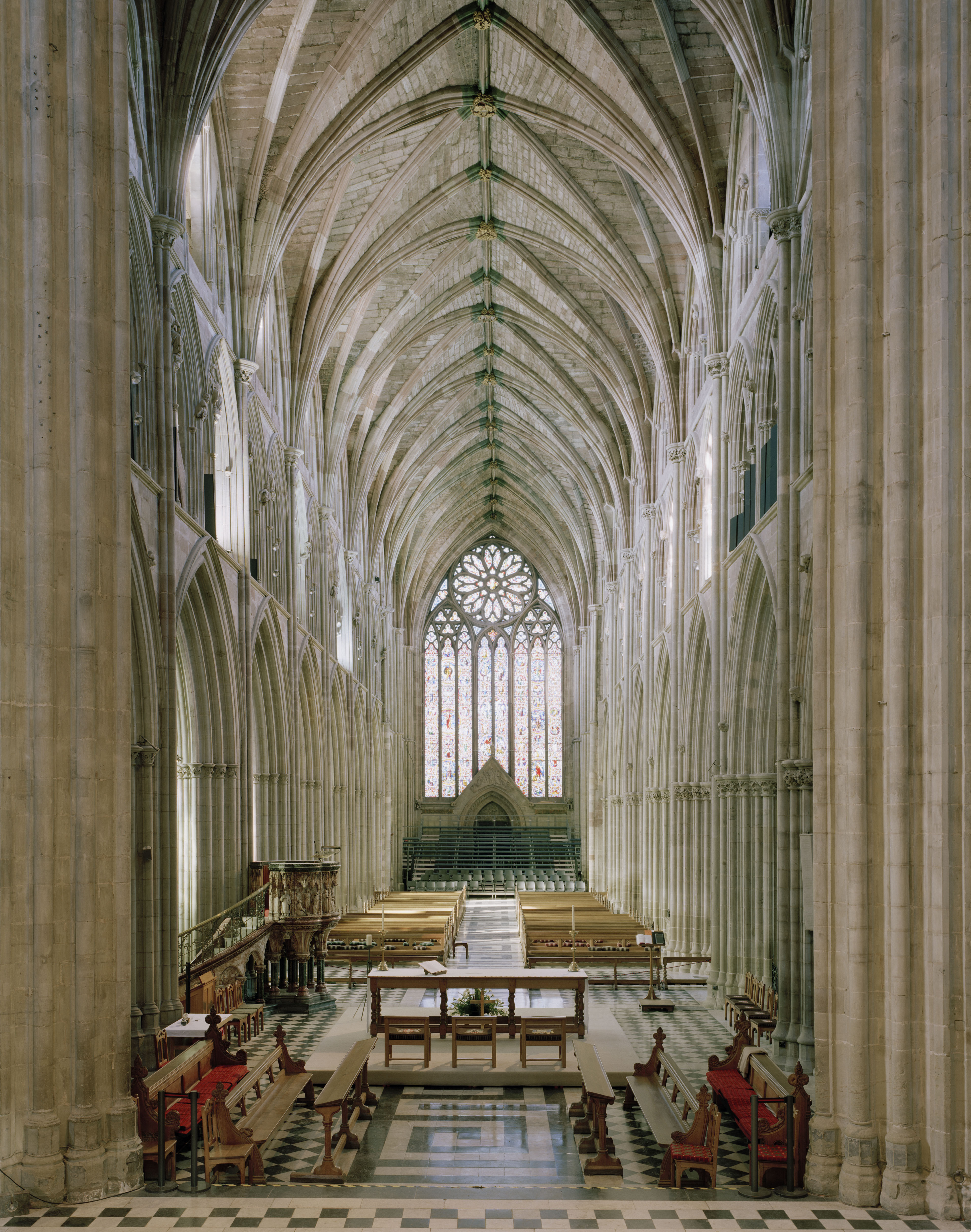 The soaring gothic nave of Worcester Cathedral, its checkered tile floor leading towards a stained-glass rose window high above the altar.