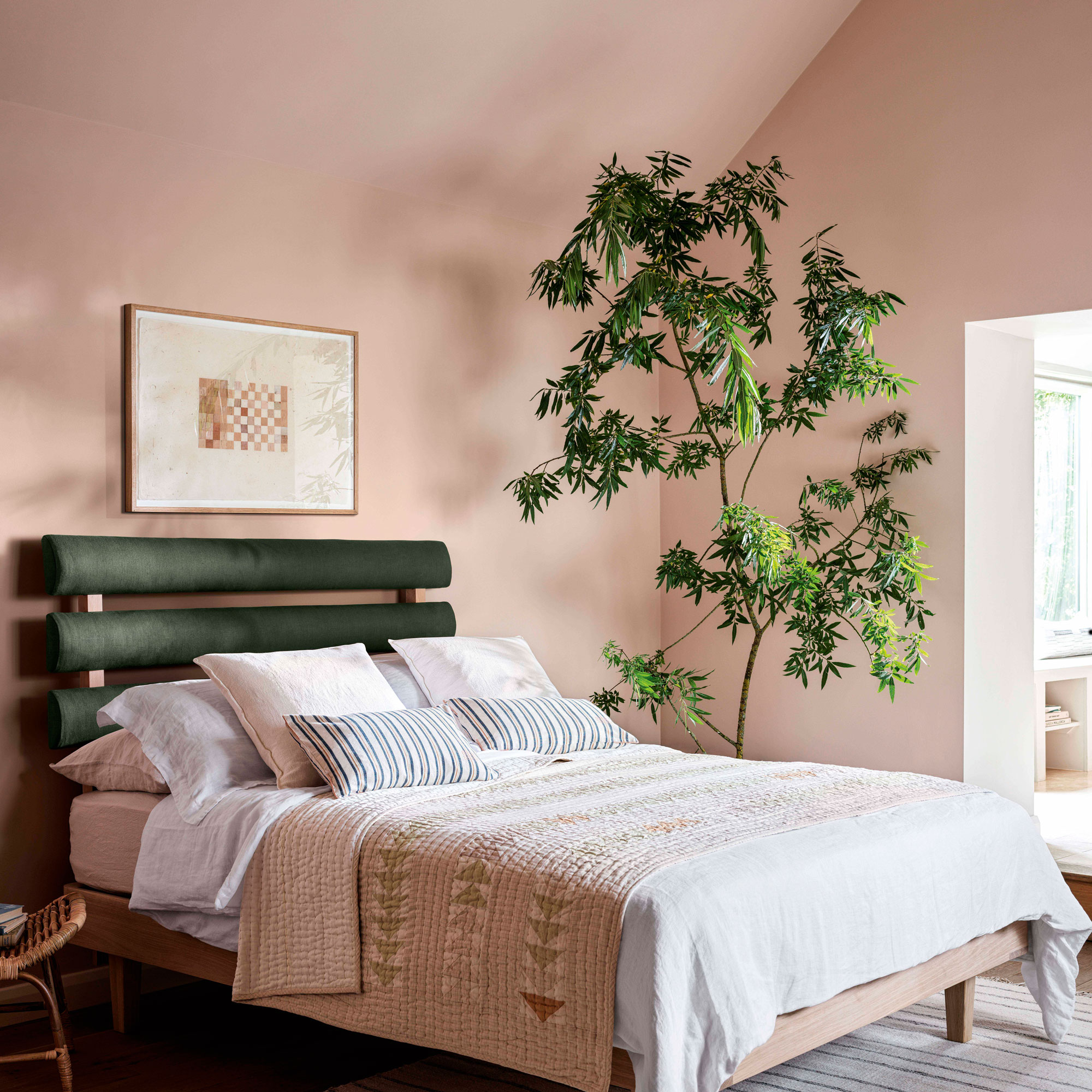 Pink bedroom with a wooden bed with pink pattern bedding on top, a large indoor tree in corner