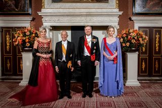 Queen Maxima wearing a red gown and diamond tiara standing next to President Marcelo Rebelo de Sousa of Portgual wearing a tuxedo, King Willem-Alexander in a tuxedo and Princess Amalia in a purple gown and red sash