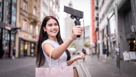 Mixed race woman traveler use camera record vlog while travel in city. Attractive female tourist feel happy and relax while walking on street, enjoy taking a photo during vacation trip in Frankfurt.