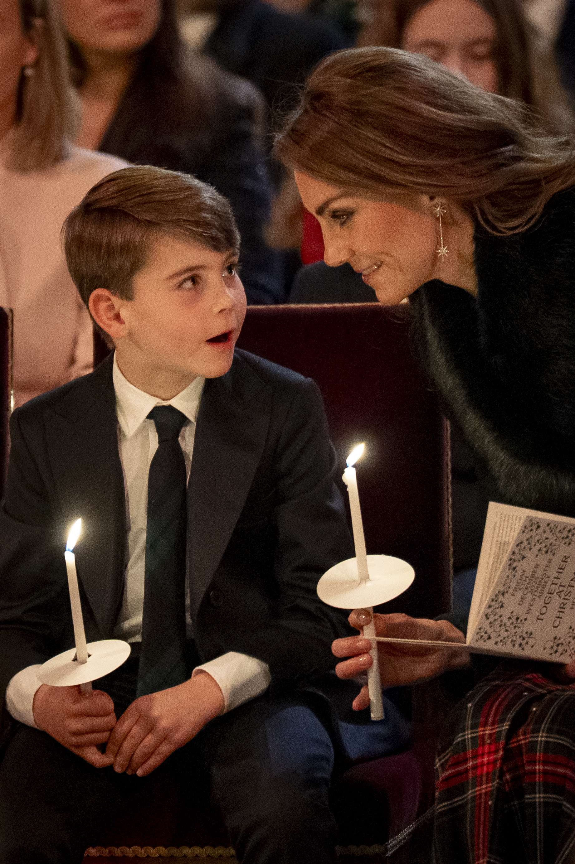 Prince Louis holding a candle sitting next to Princess Kate