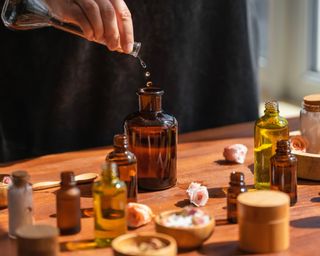 Woman concocting a solution with essential oils. Lots of different glass jars and bottles on a wooden table