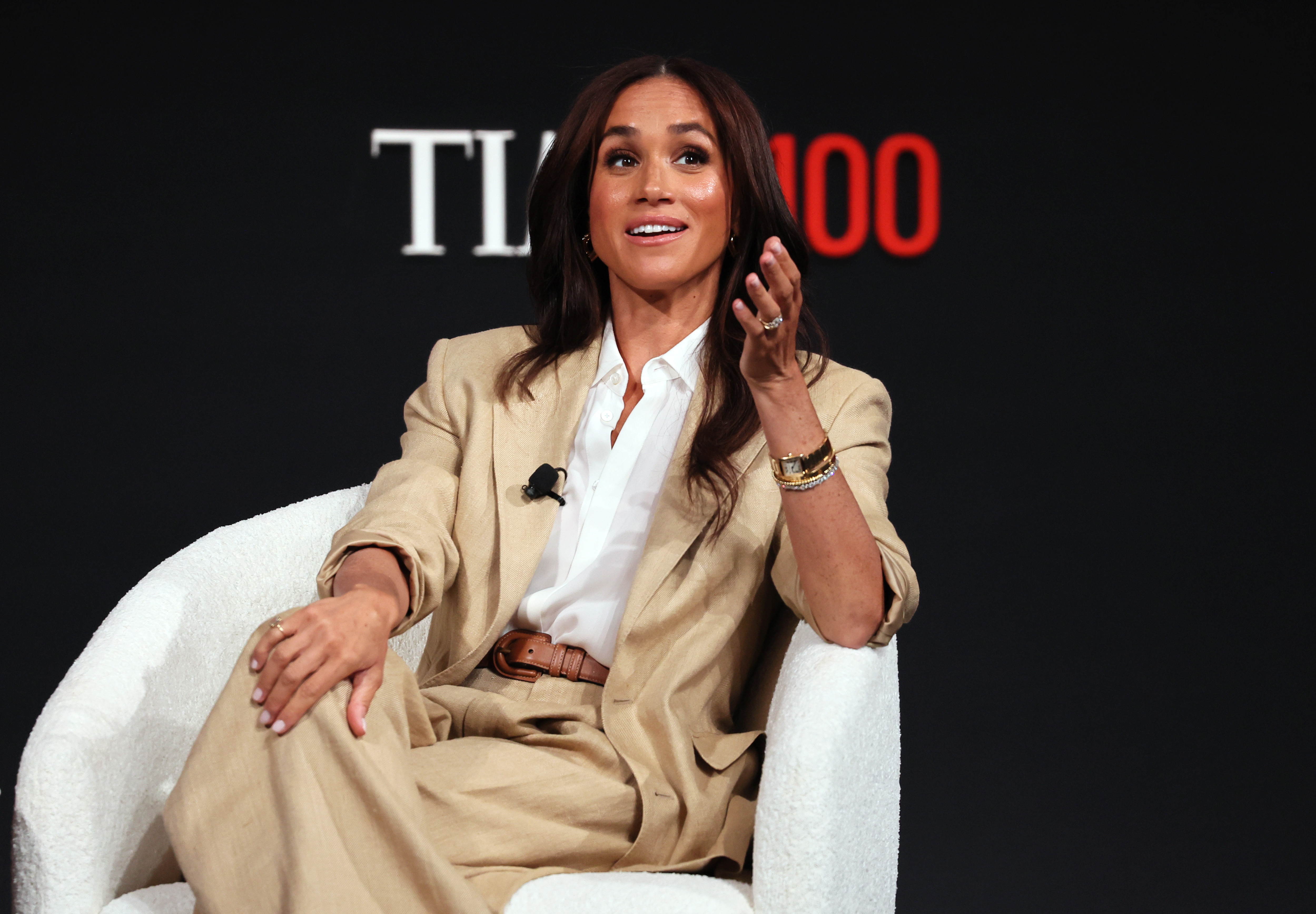 Meghan Markle wearing a tan suit talking in a chair on stage