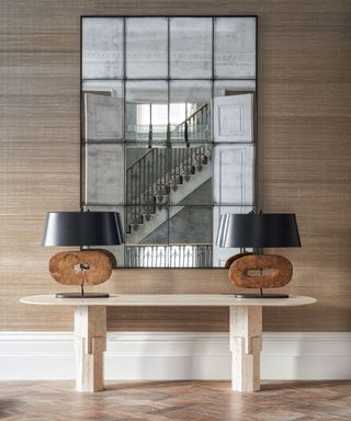 Hallway with parquet floor, console table and large mirror reflecting the staircase, two matching table lamps on table
