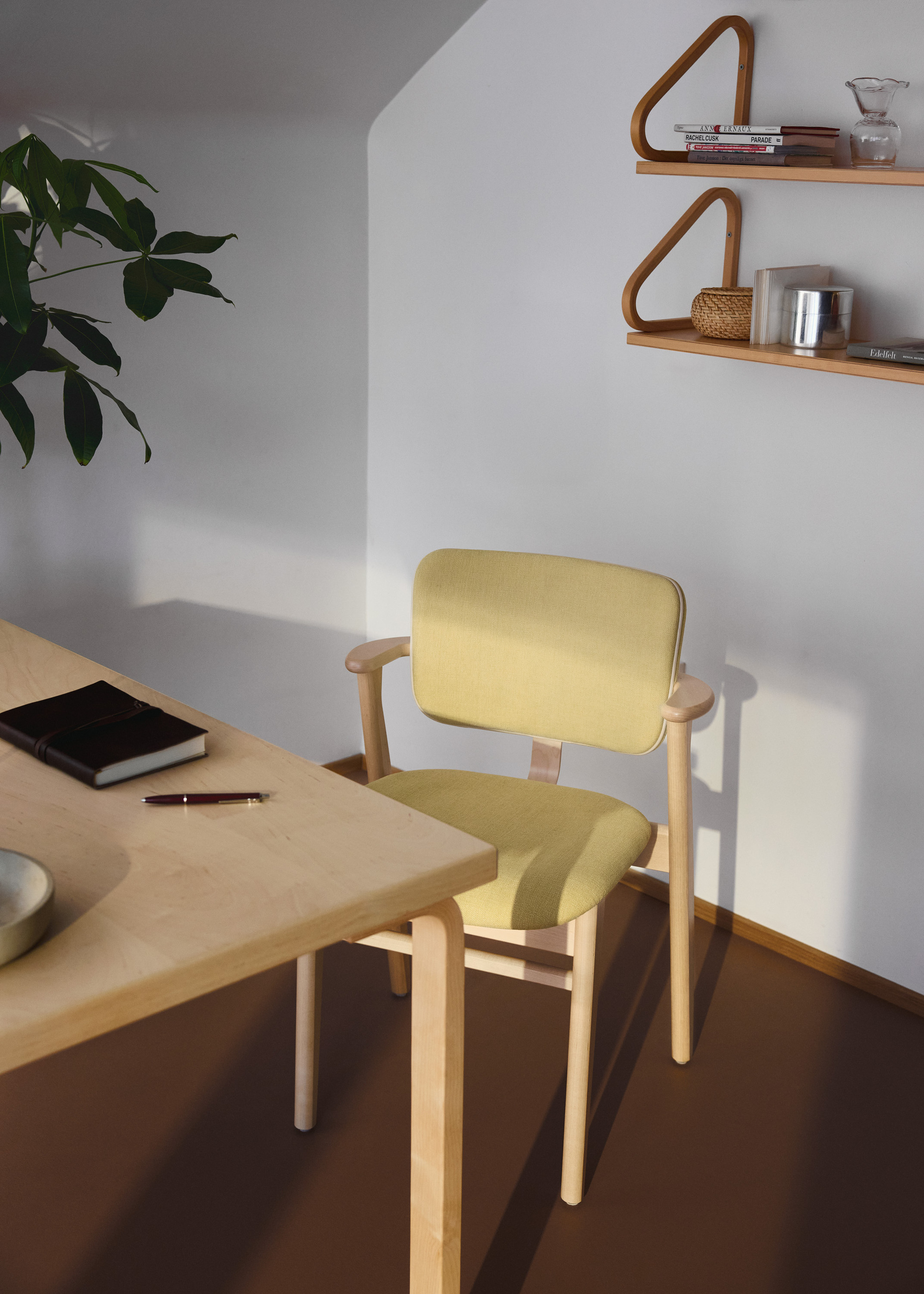 A light yellow and light wood desk chair in front of a matching wooden desk in a white office with brown carpet flooring.