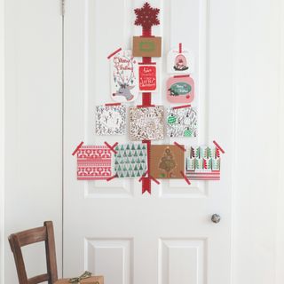 A wall Christmas tree on a white door made out of Christmas cards and tape and a felt star on top