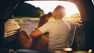 man and dog sat in boot of car