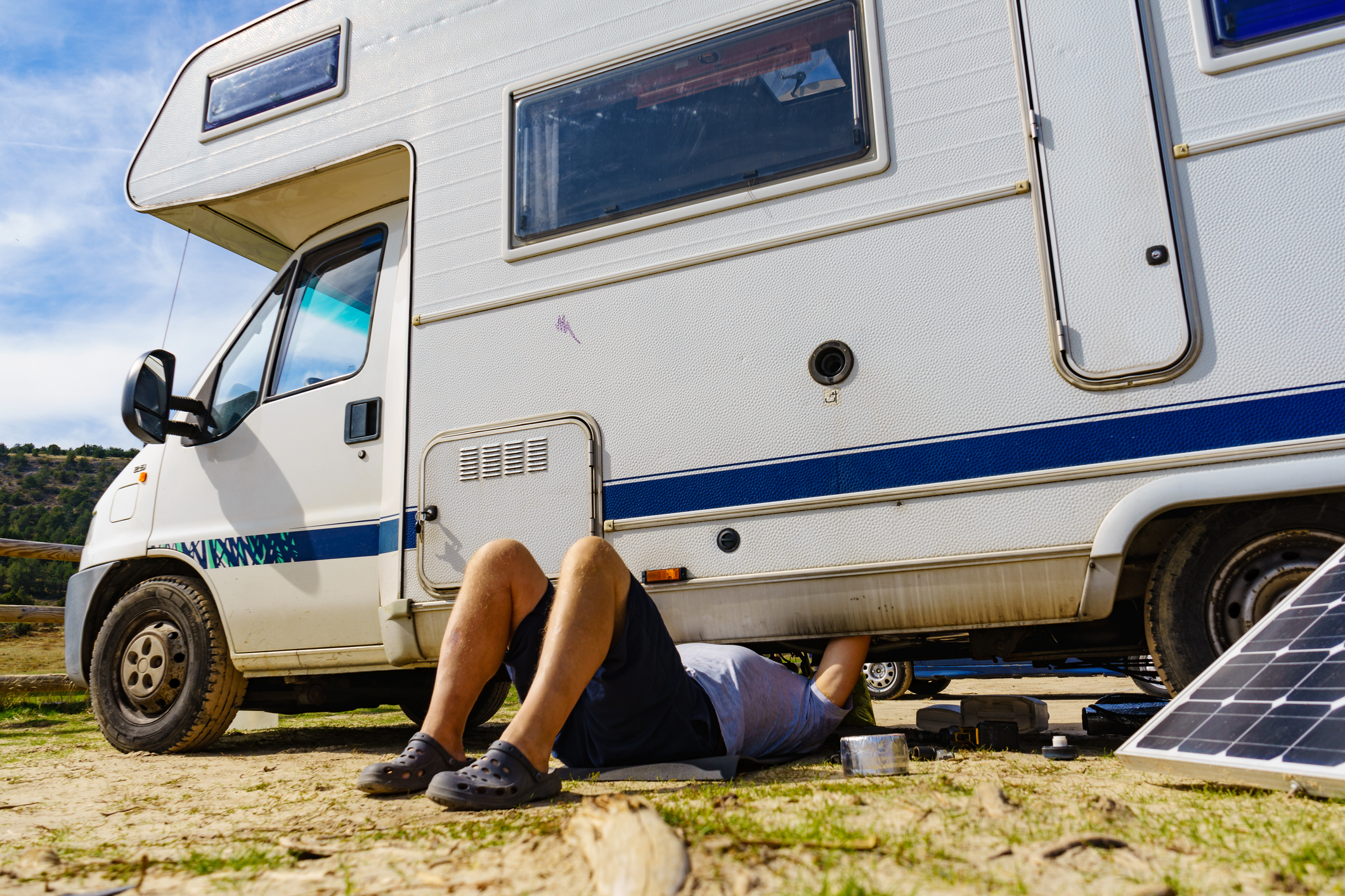 Man lying on ground, repairing bottom of an RV.