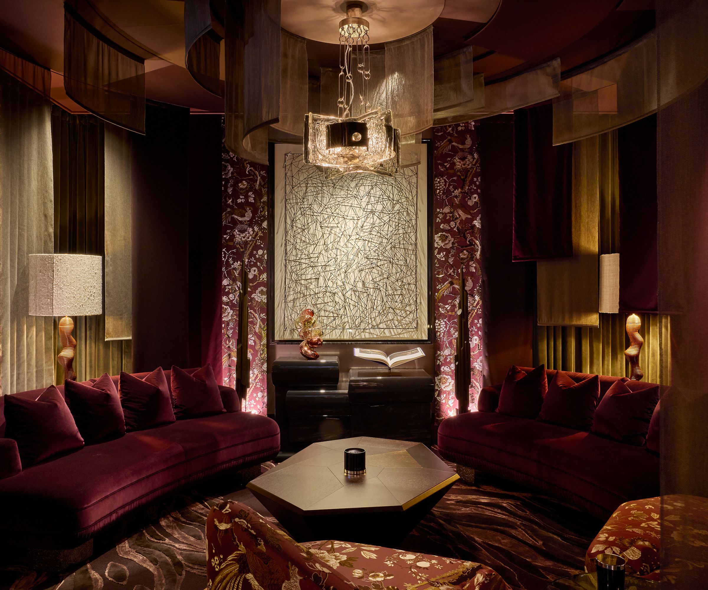 Luxurious lounge with dark purple velvet sofas, floral armchairs, gold lighting, a glass and metal chandelier pendant, and a deep purple carpet, with a large canvas at the center