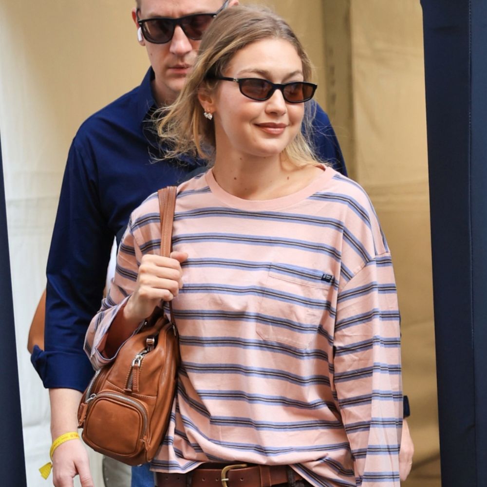 Gigi Hadid walks down the street in Milan wearing brown straight leg jeans with loafers and a striped t-shirt.