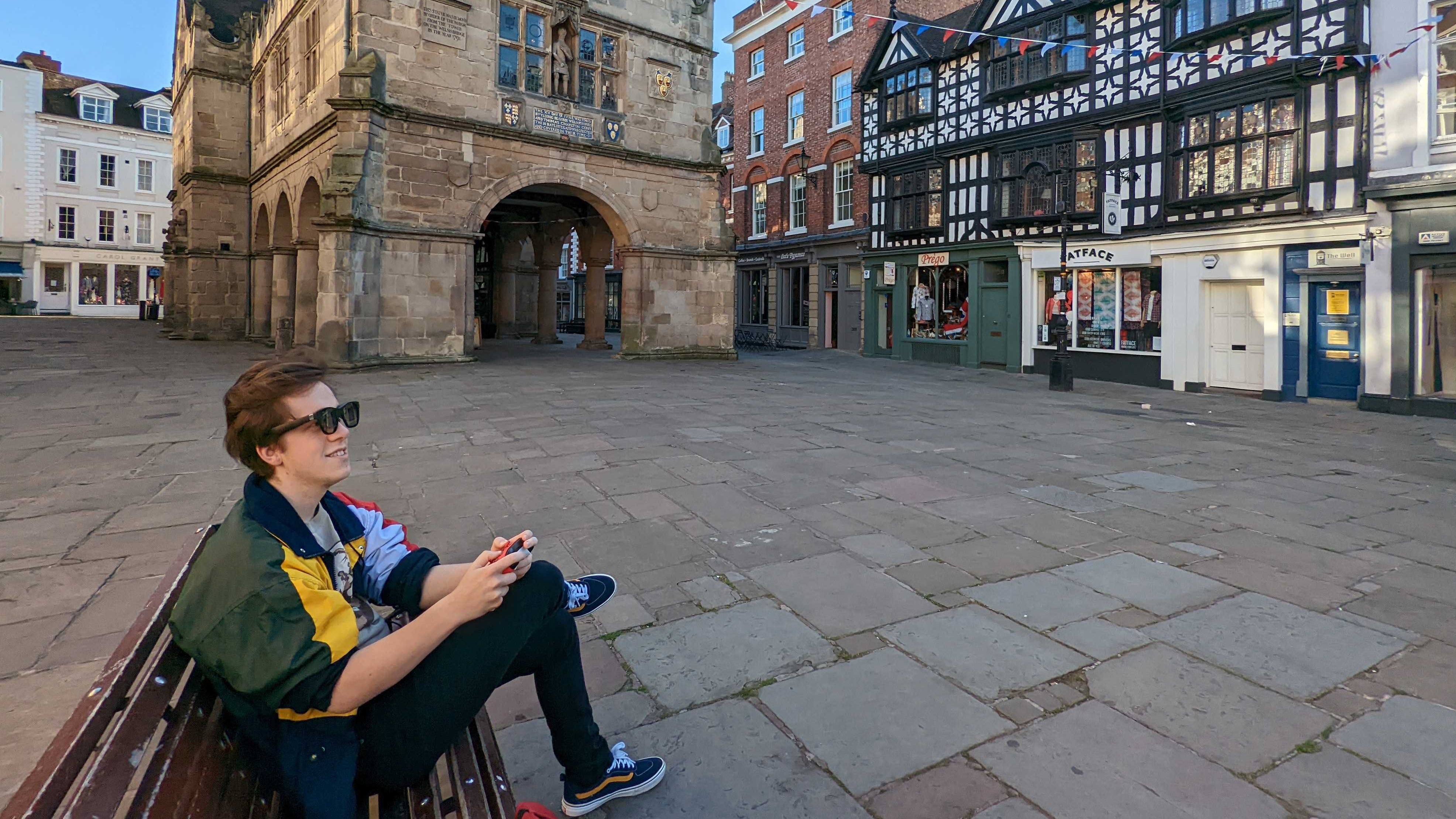 Our reviewer trying out the Xreal Air AR Glasses while sat on a bench in front of an old-looking stone building