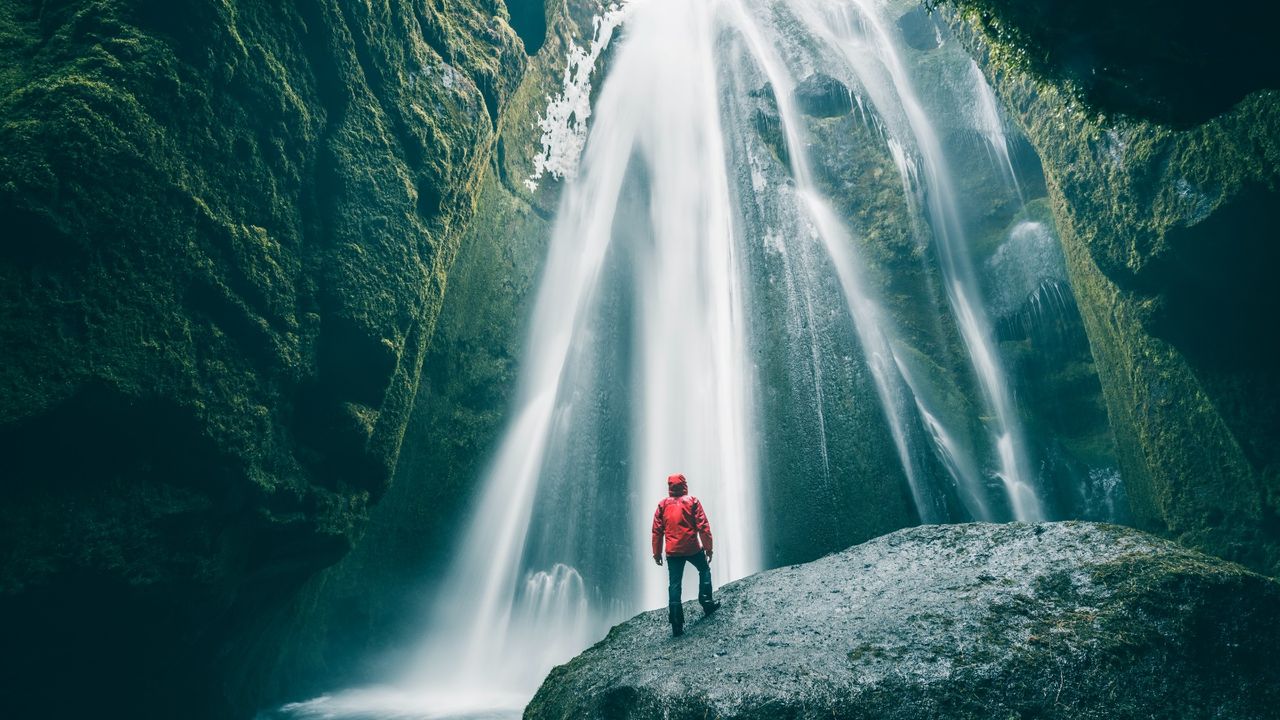 A man stands on a rock in front of a cascading waterfall in Iceland