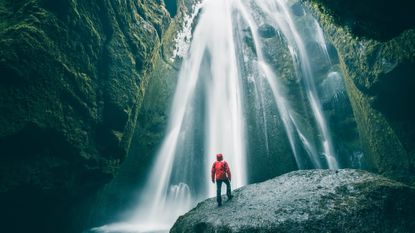 A man stands on a rock in front of a cascading waterfall in Iceland
