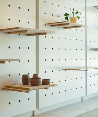 Close up view of a wall at Les Fraiseurs featuring peg board style shelving. The shelves are wooden and there is pottery on one shelf and a plant in a pot on another