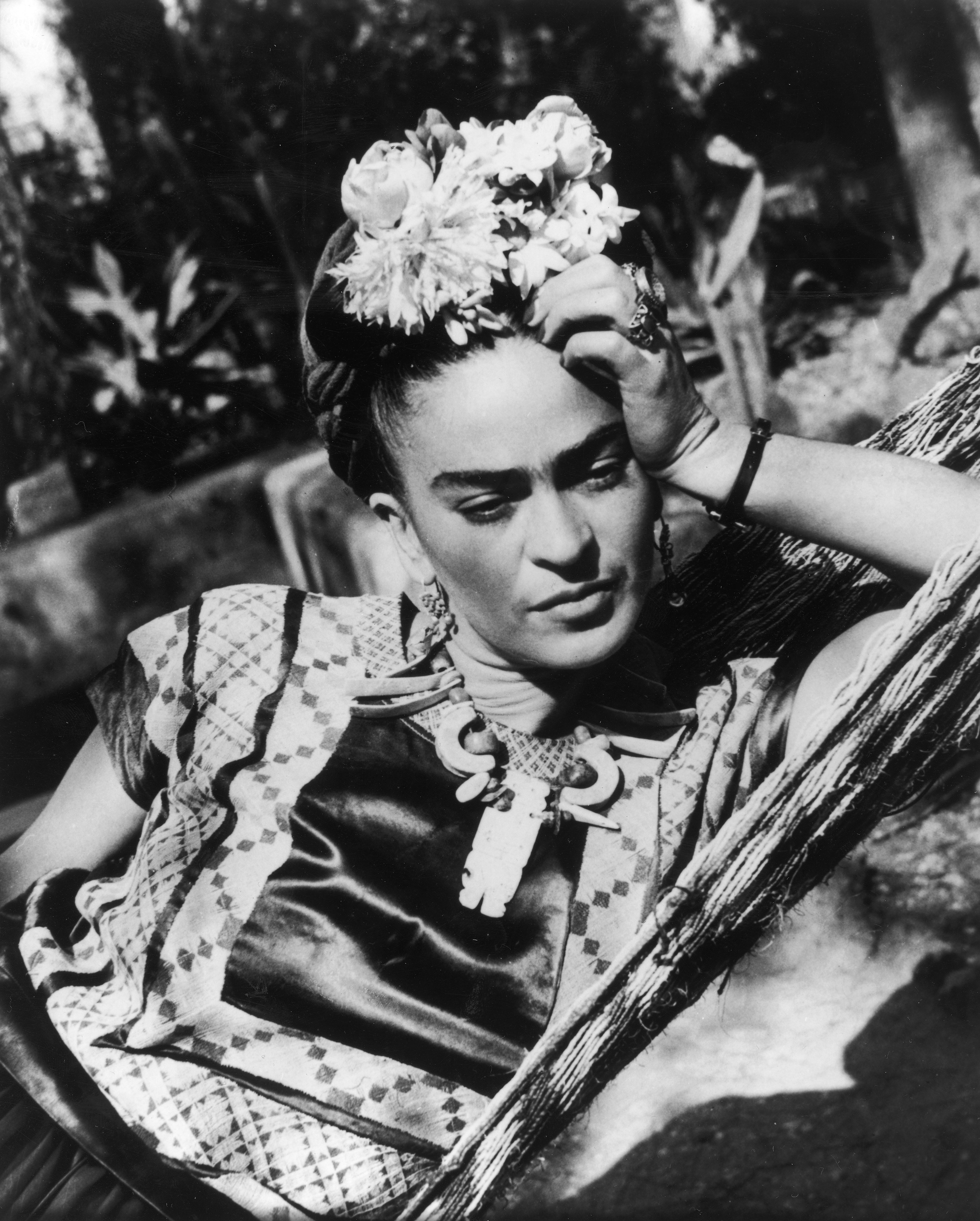 Black and white portrait of Frida Kahlo lying down with her head propped on one hand