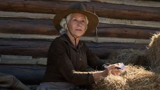 Helen Mirren as Cara Dutton sitting by hay bales looking up.