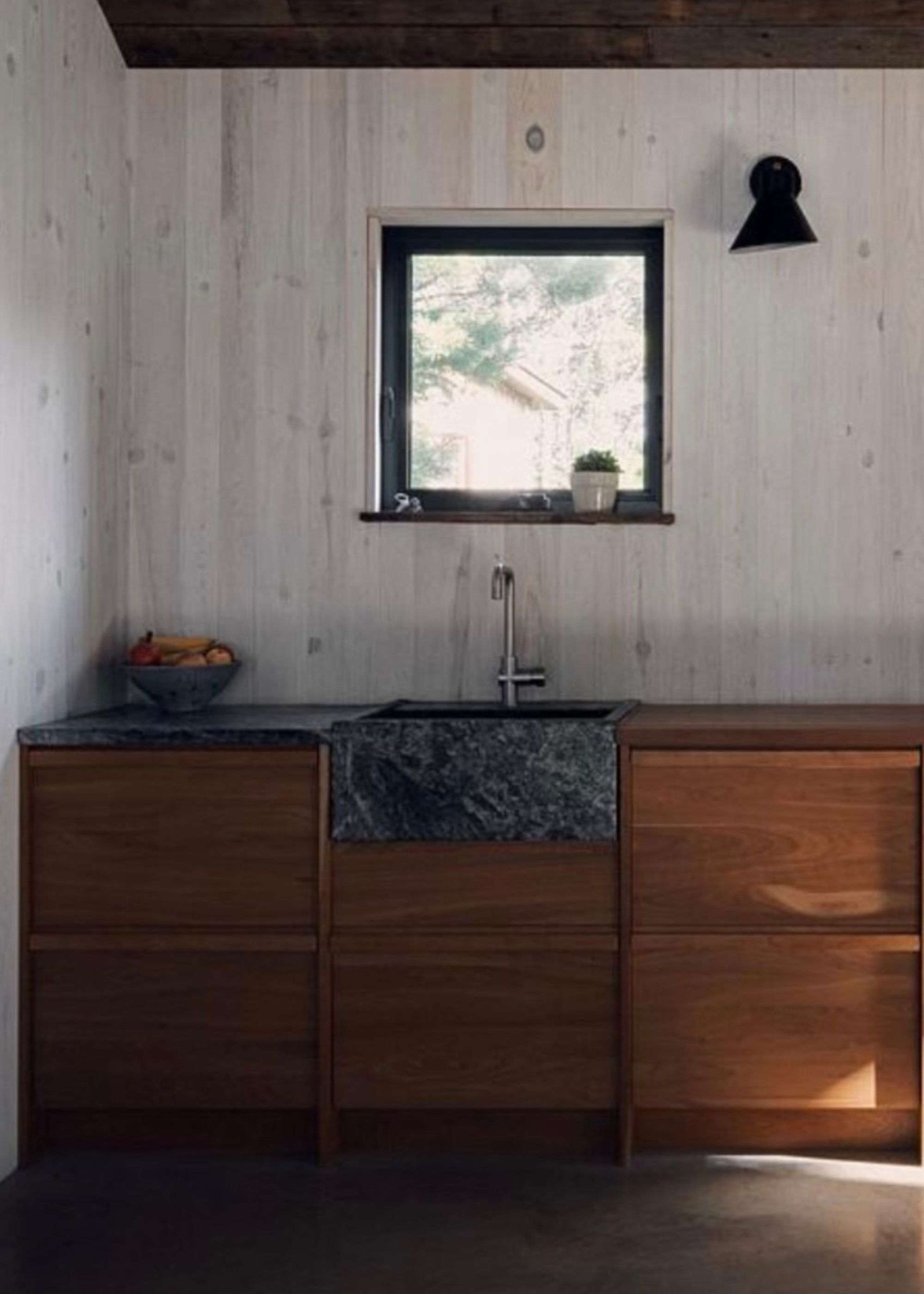 A Japanese inspired kitchen with a soapstone sink and countertop on one side of the kitchen countertop. There is also a bowl on the left side of the countertop and above the sink is a small square window looking outside