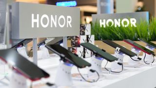 Honor smartphones shown on a retail display in an electronic store with the brand's logo in the background.
