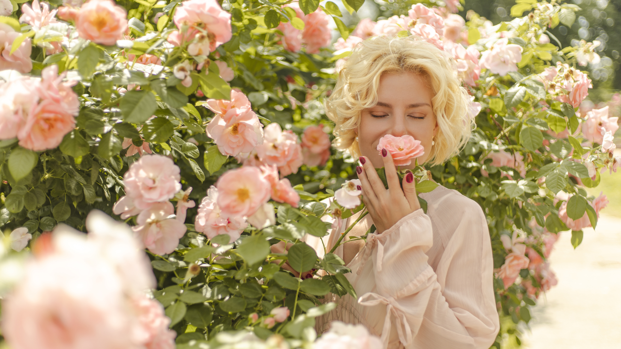 woman smelling a perfect rose with peach colored petals, inhaling its floral scent