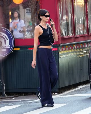 Kaia Gerber walks through New York City's SoHo neighborhood wearing a black tank top low rise navy pants and black sneakers