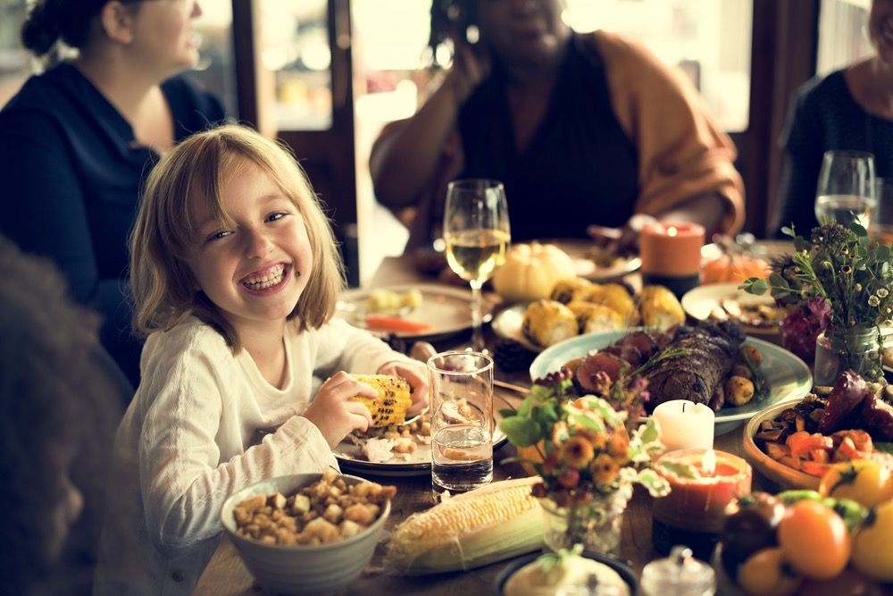 Little girl smiling and eating corn at Thanksgiving dinner.