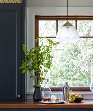 kitchen with large window, dark blue cabinet and pendant light and foliage in vase