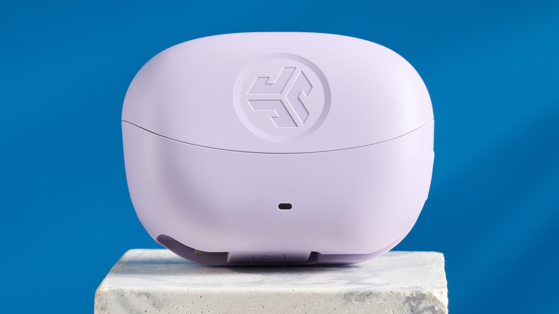 the jlab go pods anc earbuds in lilac with a lilac charging case and built in usb-c cable against a blue background on a marble stand