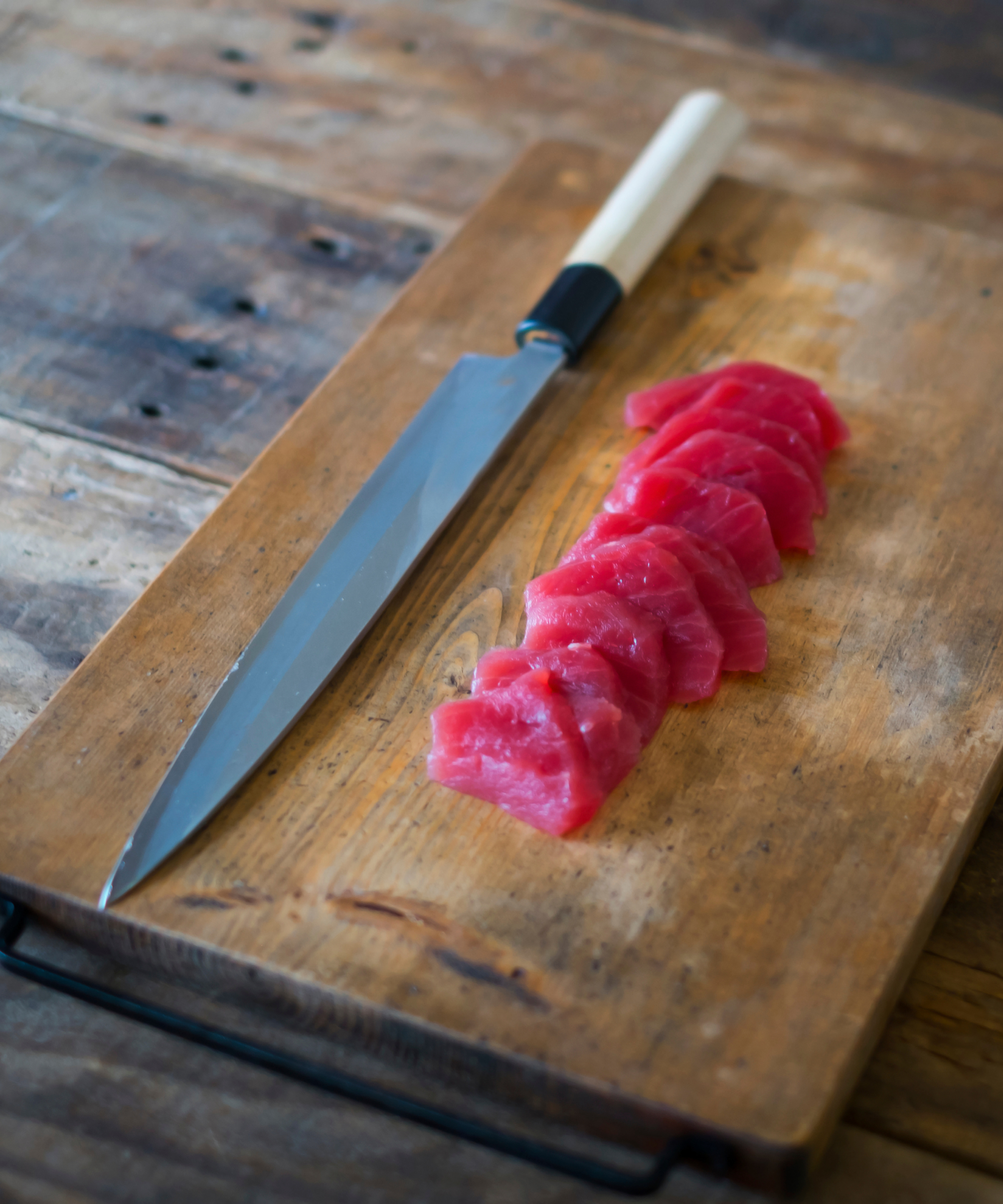 A no-brand Japanese knife on a cutting board next to sliced tuna sashimi
